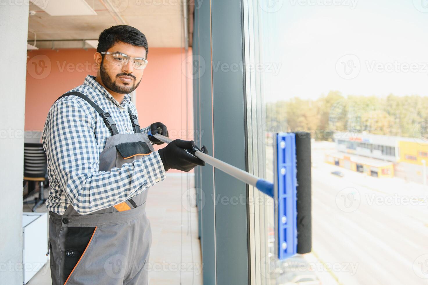 An Indian cleaning service worker washes windows in an office building photo