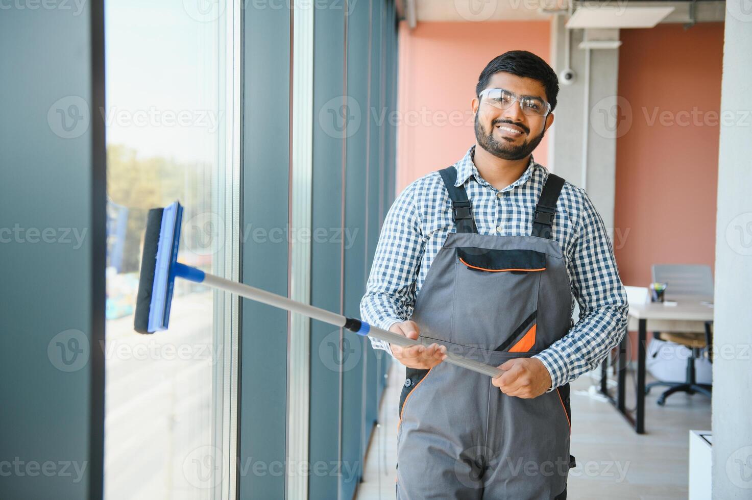 An Indian cleaning service worker washes windows in an office building photo