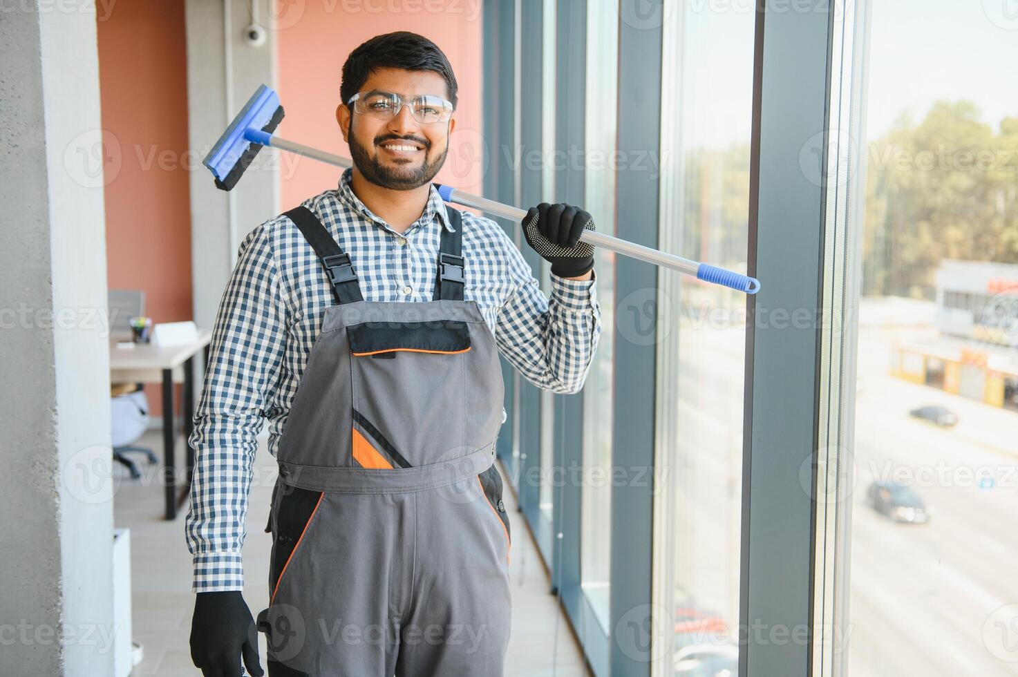 An Indian cleaning service worker washes windows in an office building photo