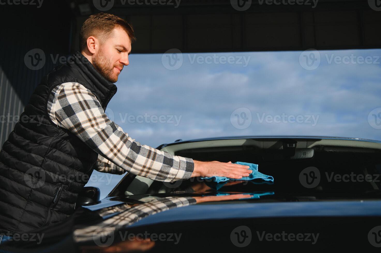 A man wipes his car with a microfiber towel after washing it at a car wash photo
