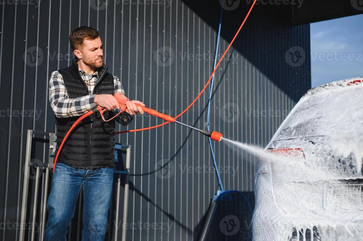 Car wash equipment. A man is washing a car at self service car wash. High pressure vehicle washer machine sprays foam photo