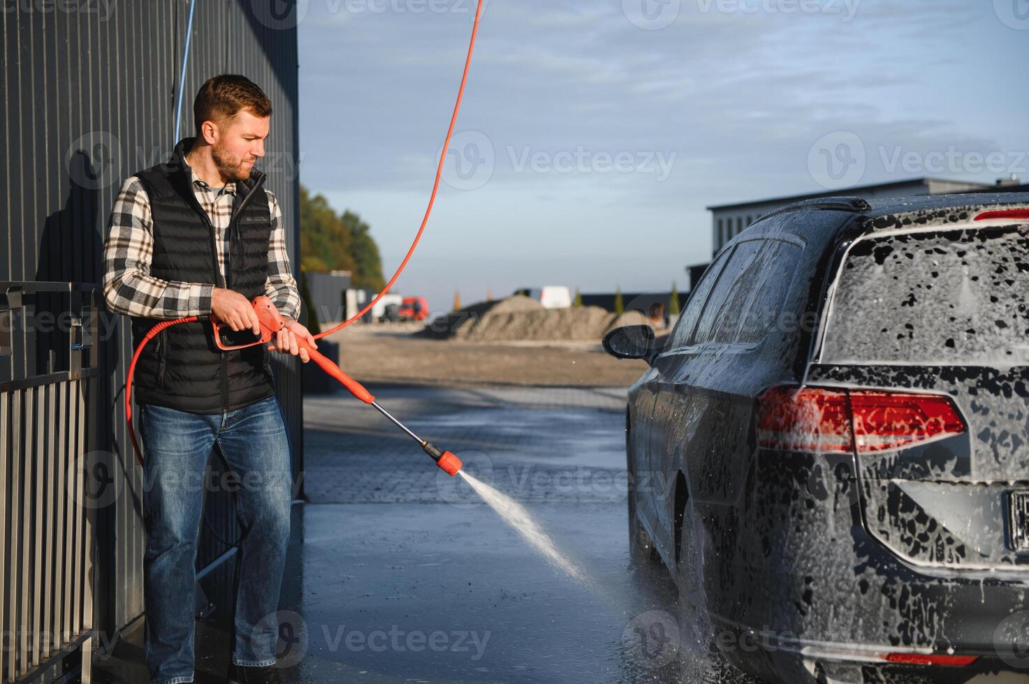 Car wash equipment. A man is washing a car at self service car wash. High pressure vehicle washer machine sprays foam photo