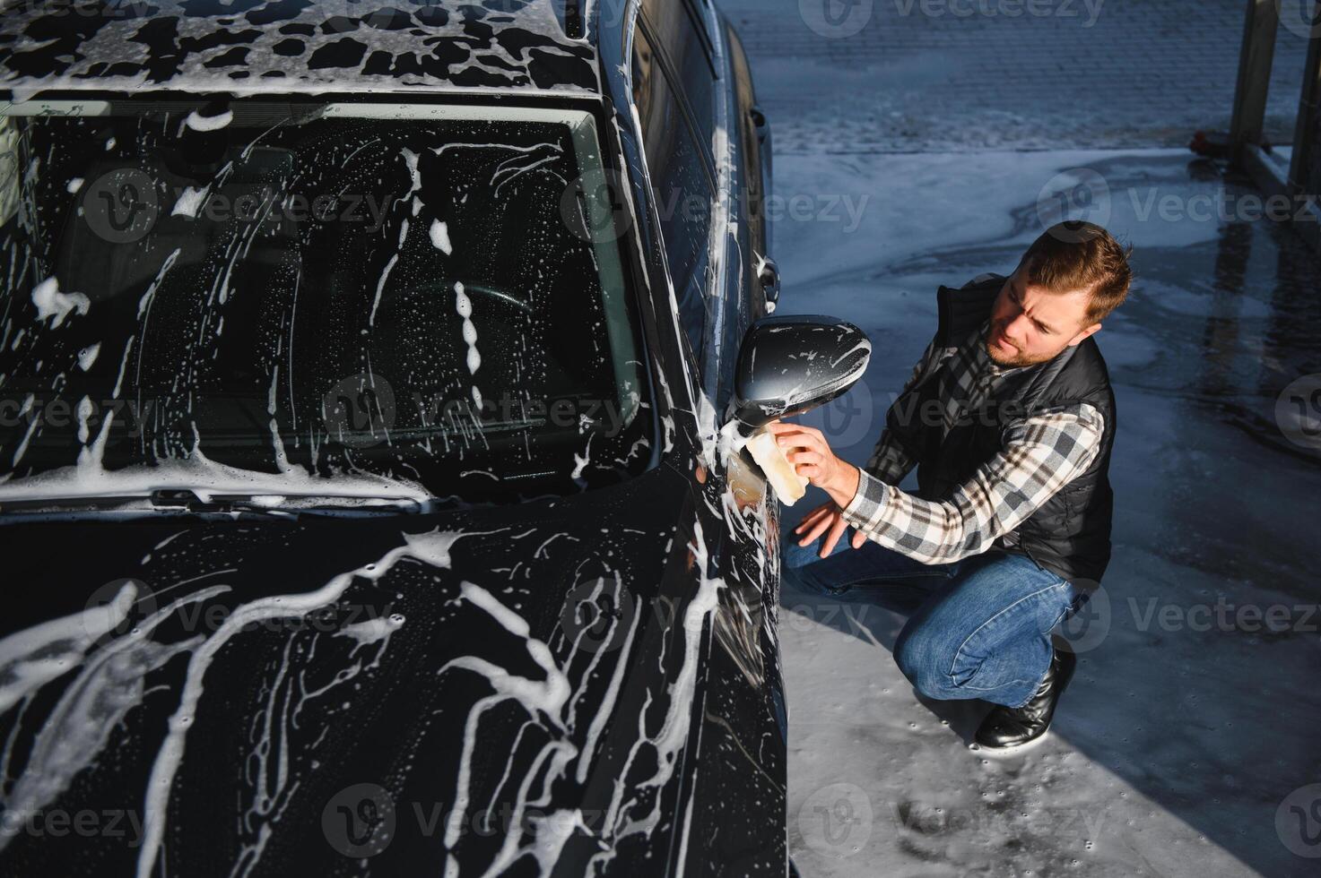 Man worker with a sponge washes a car with foam. Car wash and car care photo