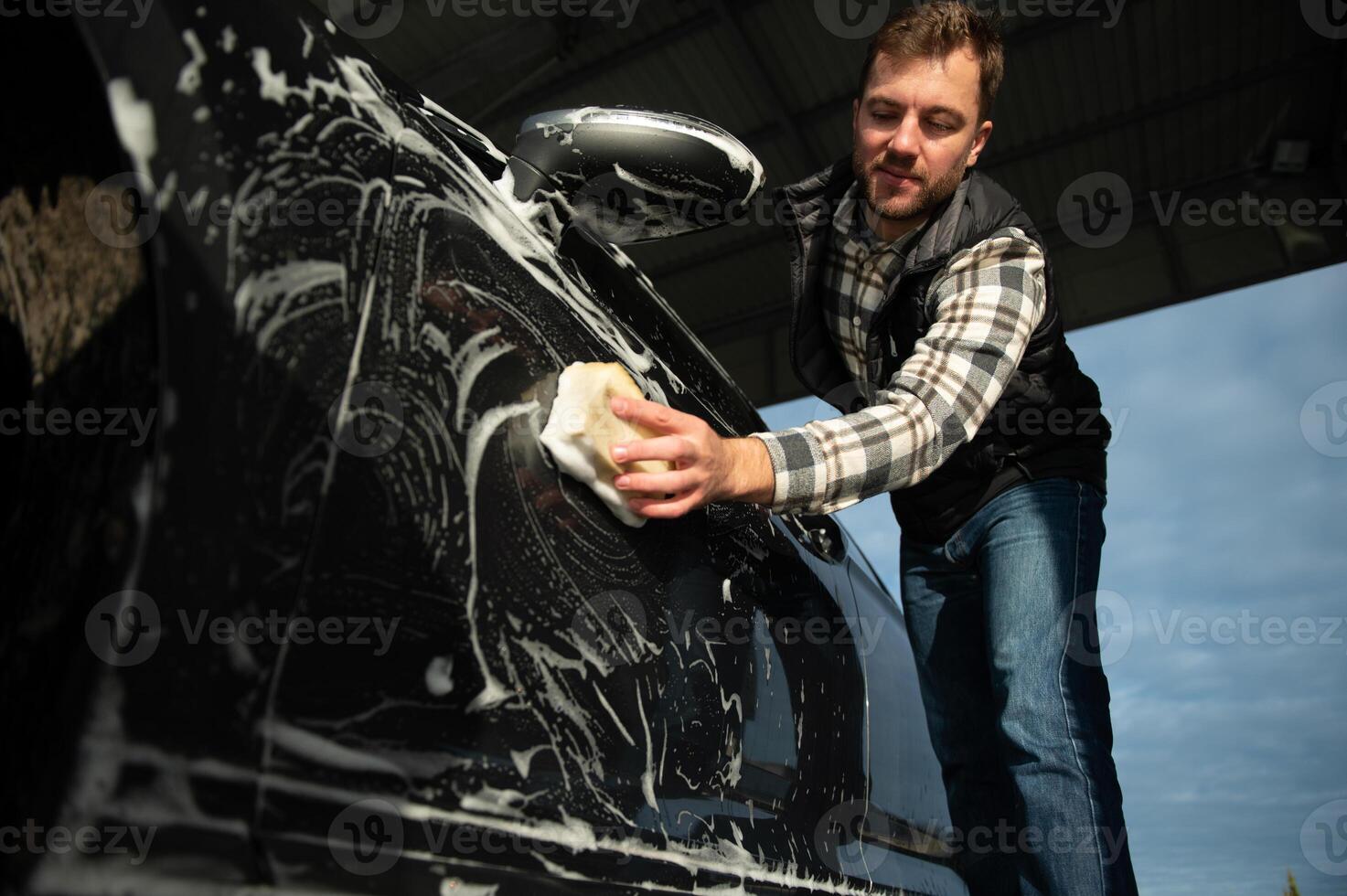 A man washes a car with a sponge at a self-service car wash photo