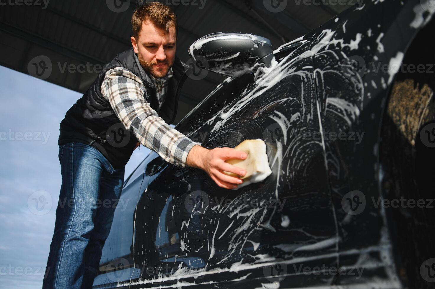 A man washes a car with a sponge at a self-service car wash photo