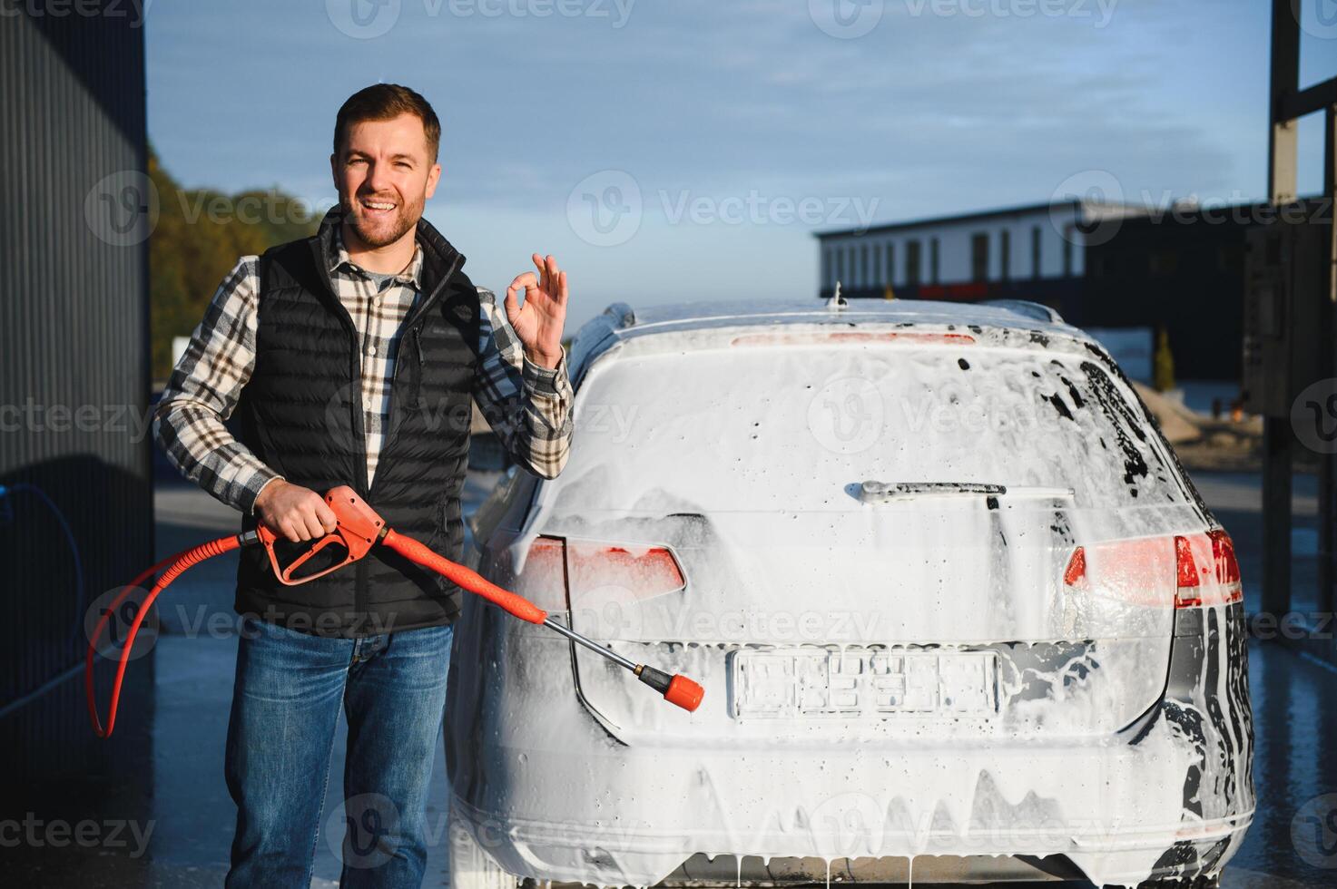 Car wash equipment. A man is washing a car at self service car wash. High pressure vehicle washer machine sprays foam photo