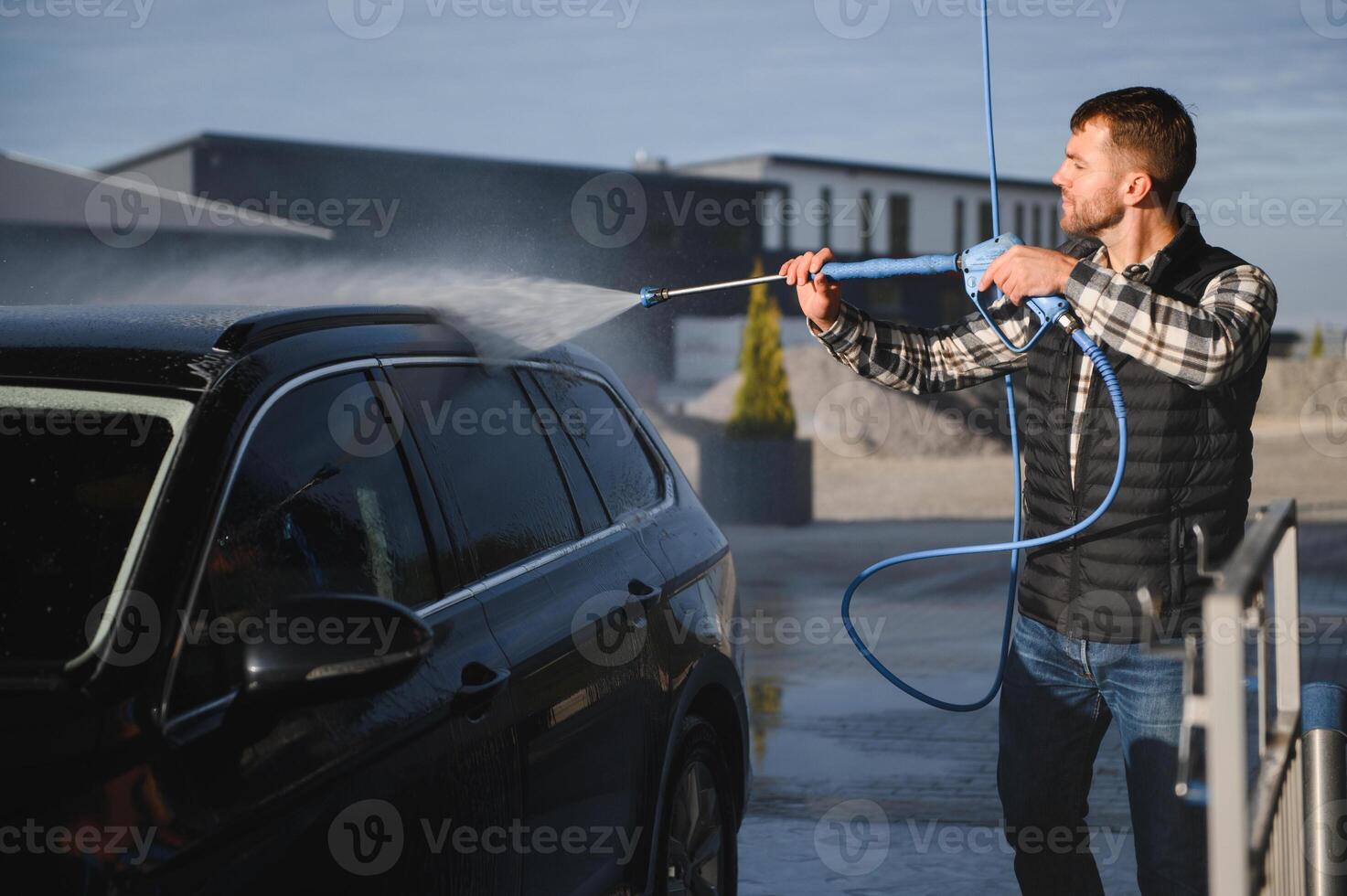 A man washes his car at a self service car wash using a hose with pressurized water. photo