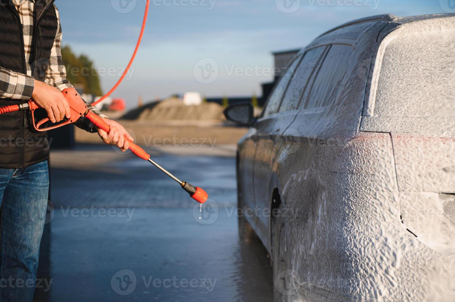 A man washes off the foam while washing the car. A vehicle is engulfed in soapy foam during a car wash, covering the tires, wheels, hood, and entire exterior of the car photo