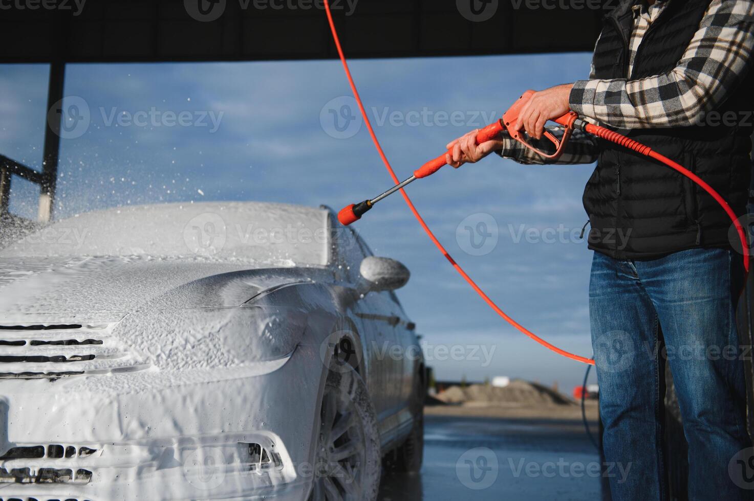 A man washes off the foam while washing the car. A vehicle is engulfed in soapy foam during a car wash, covering the tires, wheels, hood, and entire exterior of the car photo
