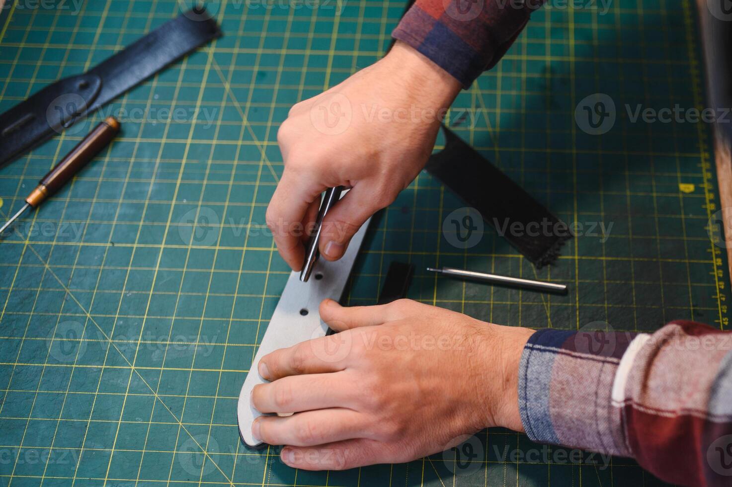 male artisan carefully punching piece of leather at professional leather workshop photo