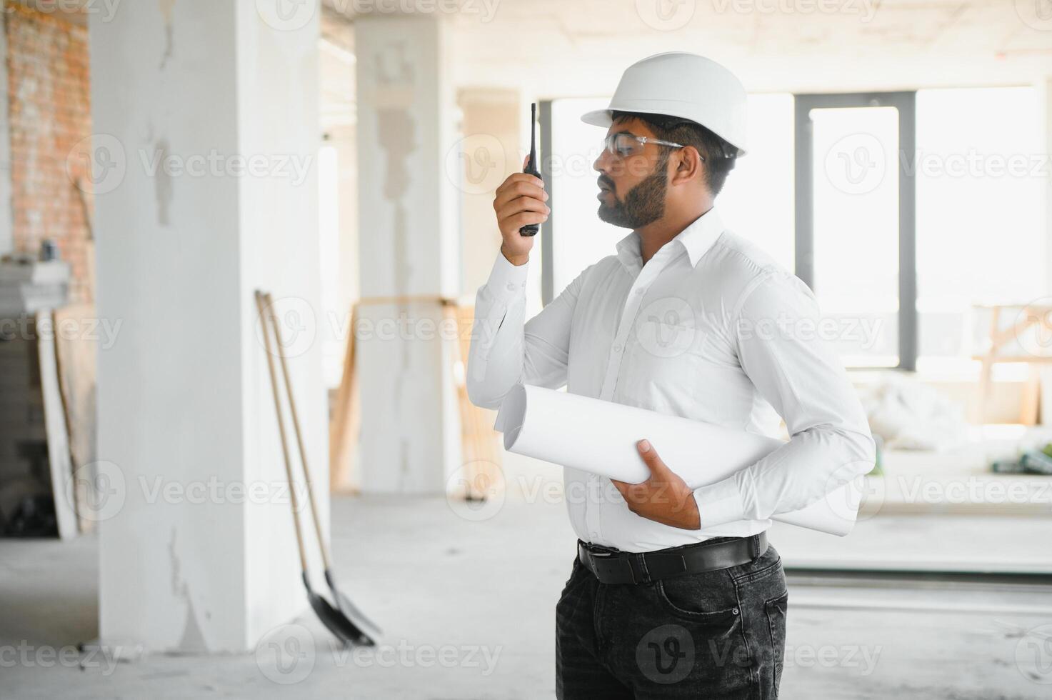 Portrait of young handsome Indian male civil engineer or architect wearing helmet at construction site photo