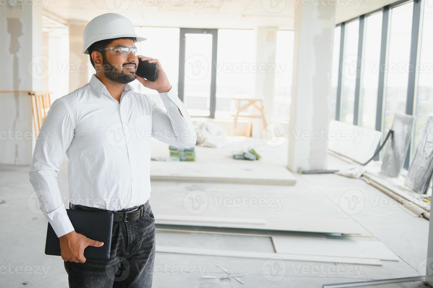 Indian construction site manager standing wearing helmet, thinking at construction site. Portrait of mixed race manual worker or architect photo