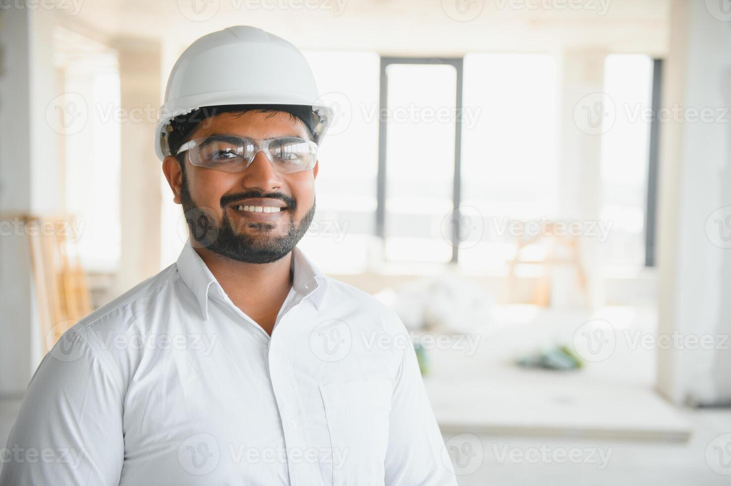 Portrait of young handsome Indian male civil engineer or architect wearing helmet at construction site photo