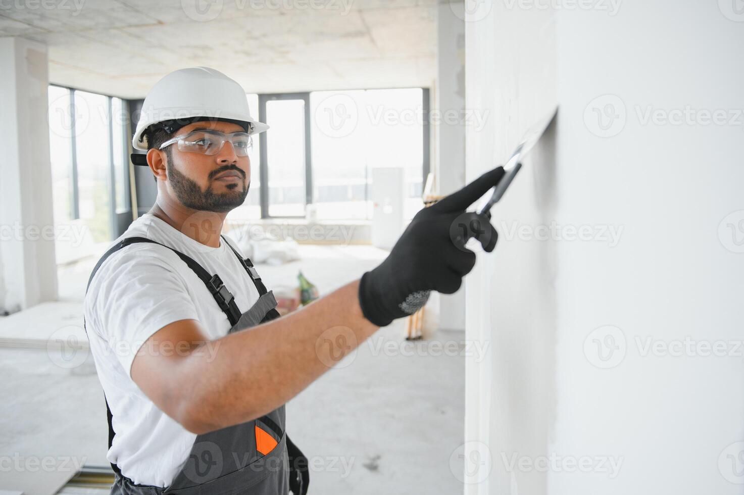 Indian Male builder in work overalls plastering a wall using a construction trowel. photo