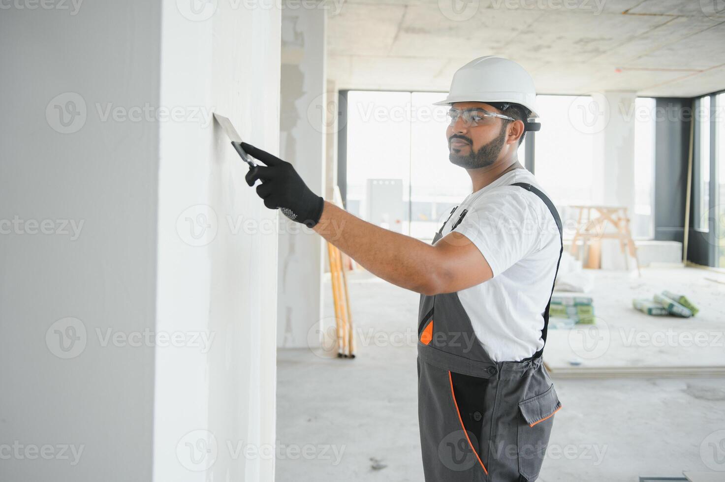 Indian Male builder in work overalls plastering a wall using a construction trowel. photo
