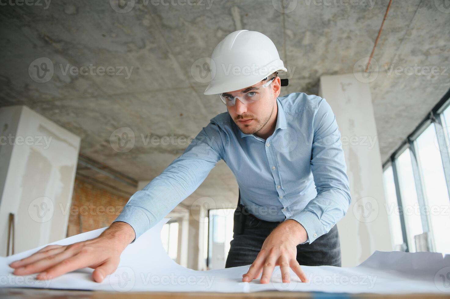 Portrait of an architect builder studying layout plan of the rooms, civil engineer working with documents on construction site photo