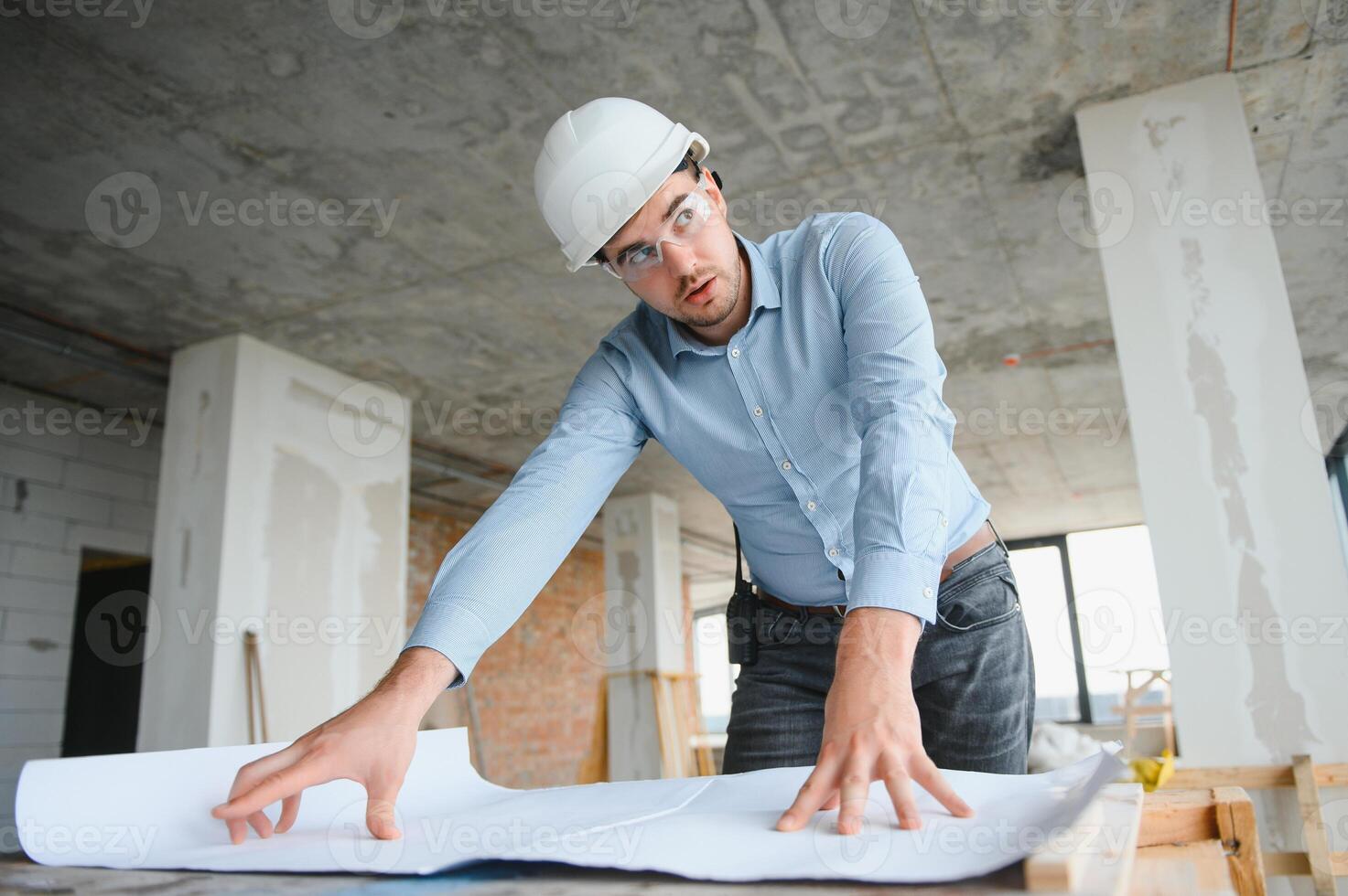 Portrait of an architect builder studying layout plan of the rooms, civil engineer working with documents on construction site photo