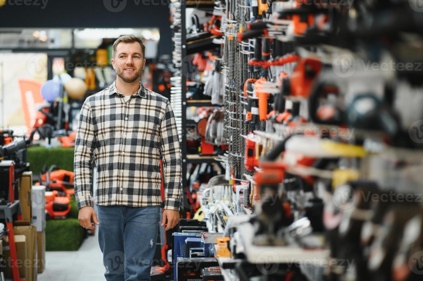 Confident smiling salesman on foreground in power tools store. Guy is ready to help clients on background photo