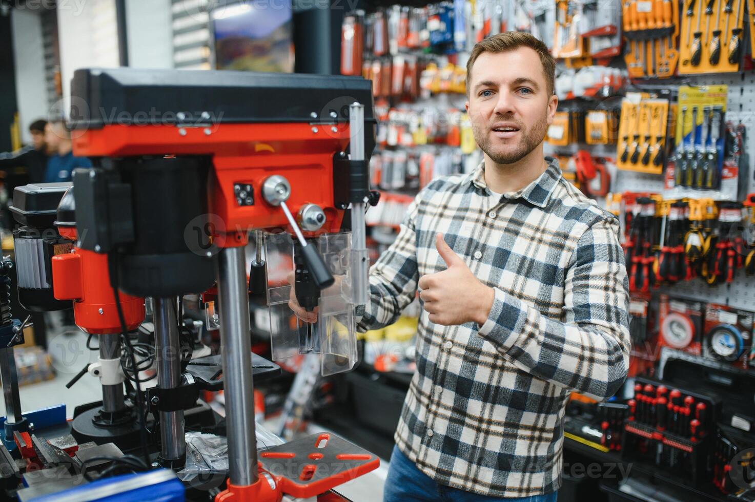 Confident smiling salesman on foreground in power tools store. Guy is ready to help clients on background photo