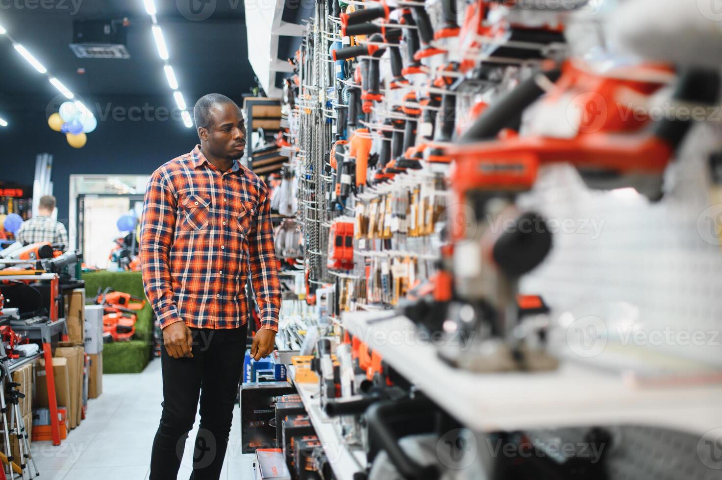 African american man holding and choosing electric screwdriver, standing in construction store photo