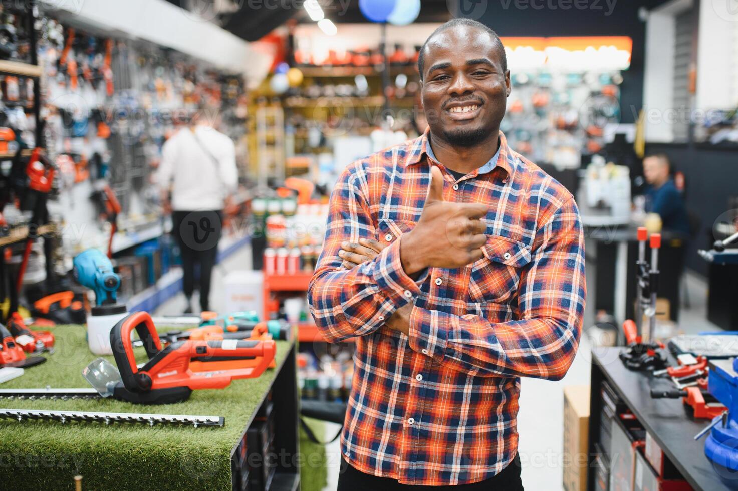 Confident smiling salesman on foreground in power tools store. Guy is ready to help clients on background photo