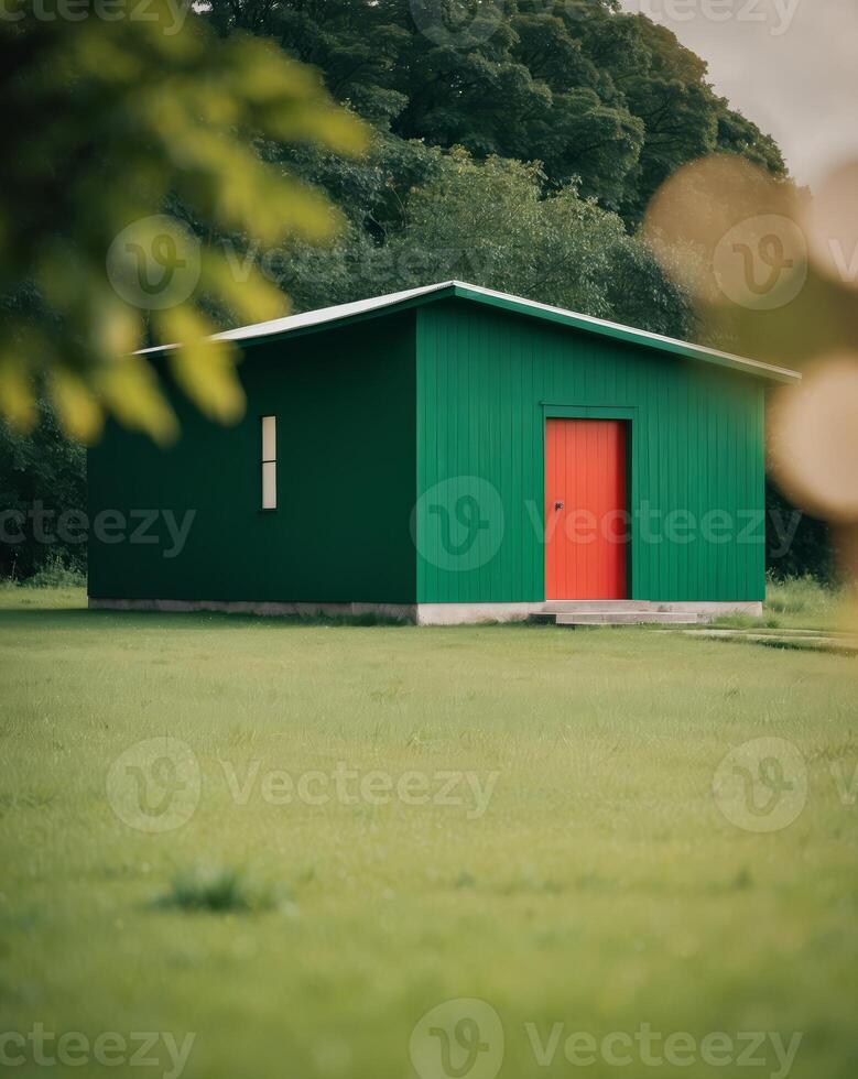 A green building with a red door sits in a field photo