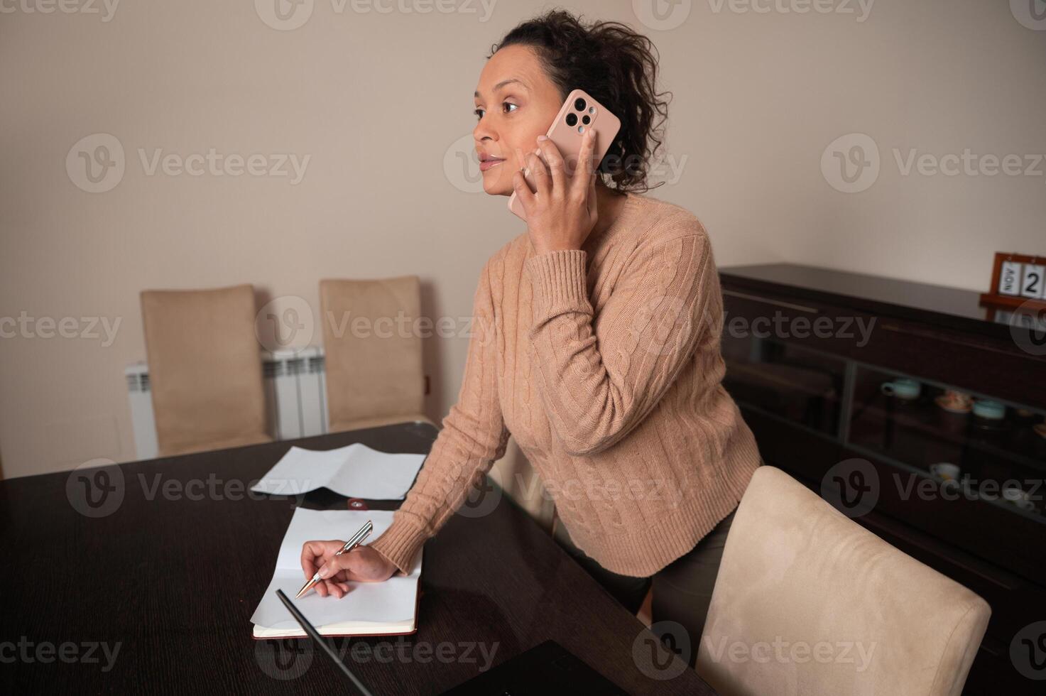 Woman multitasking at home, talking on phone and taking notes photo