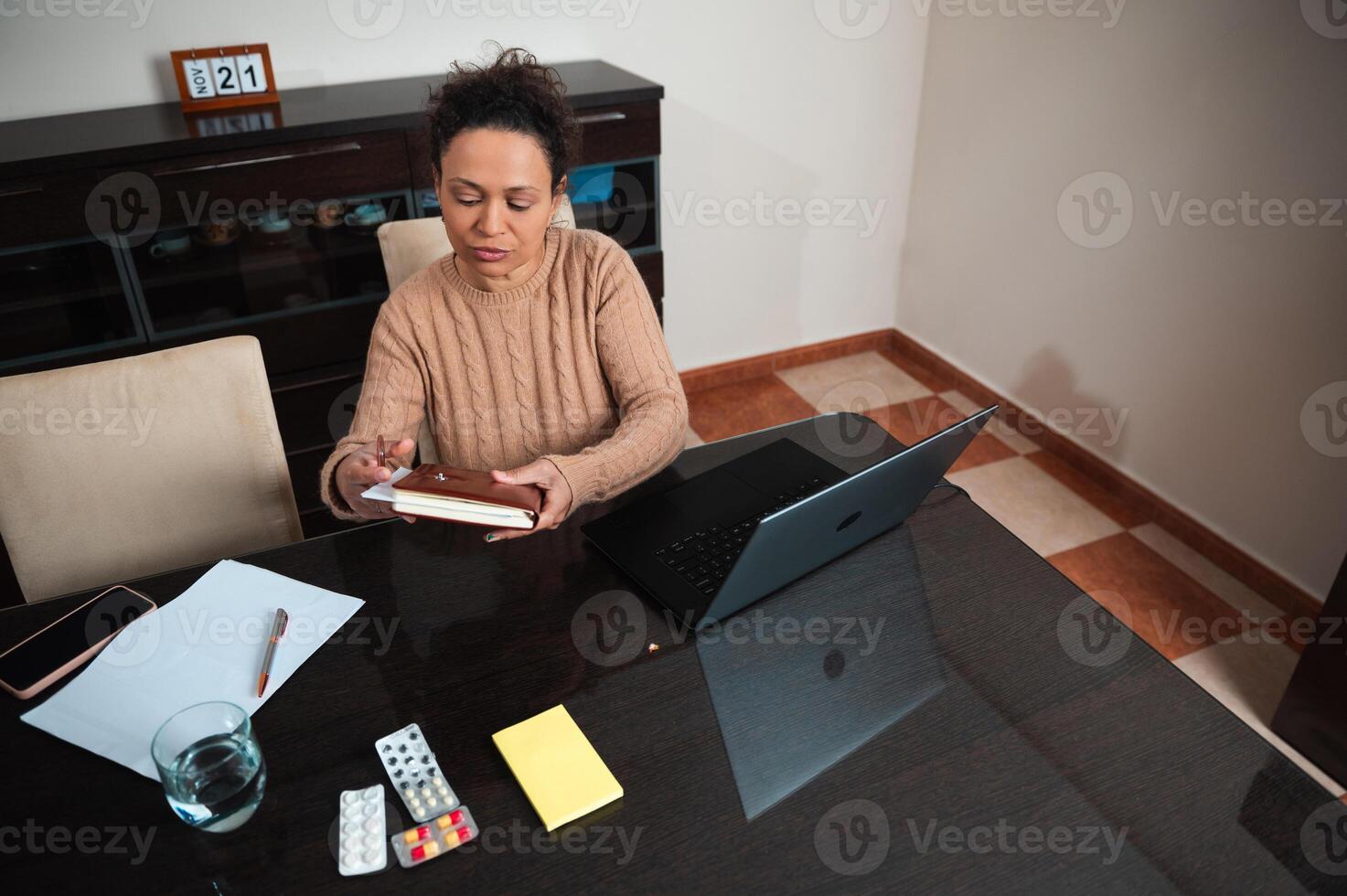 Woman working from home with a laptop and planner at table photo