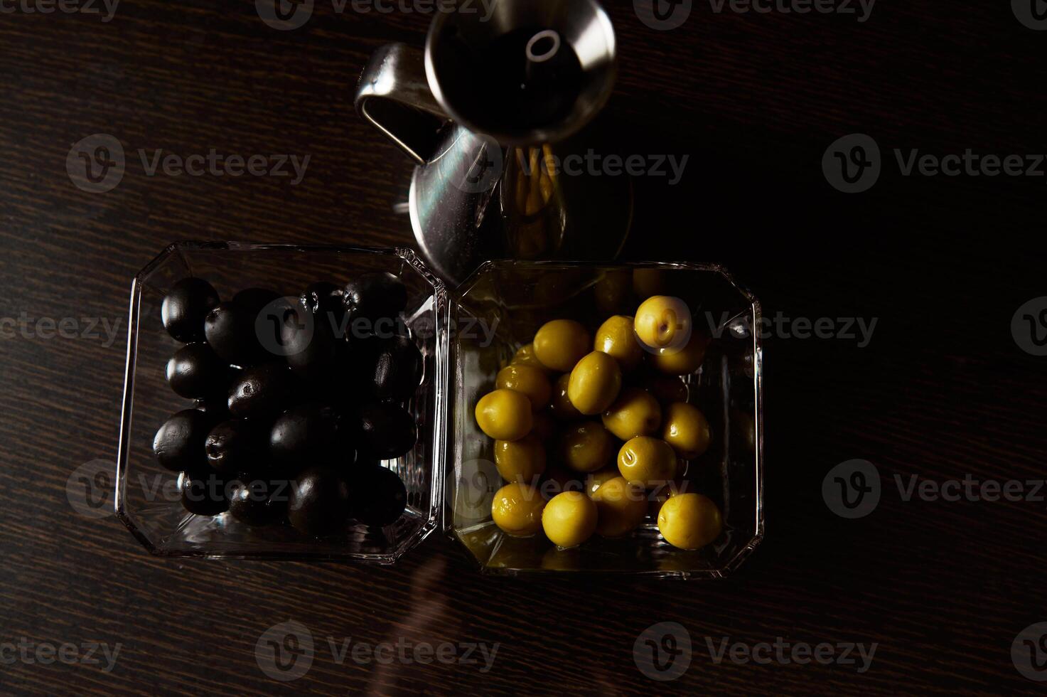 Black and green olives in glass bowls with silver oil jug photo