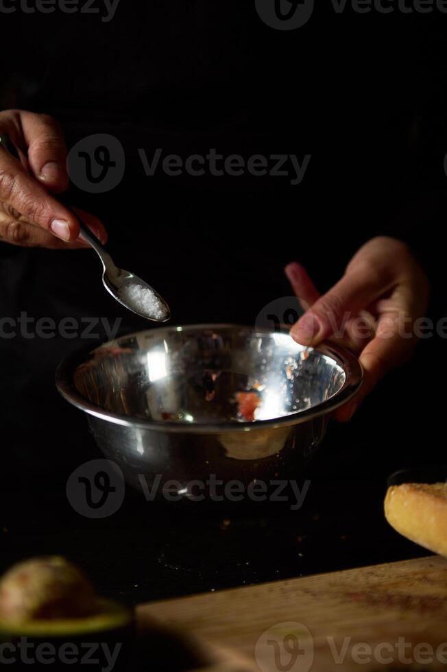 Hand adding salt to metal bowl during cooking preparation in dim lighting photo