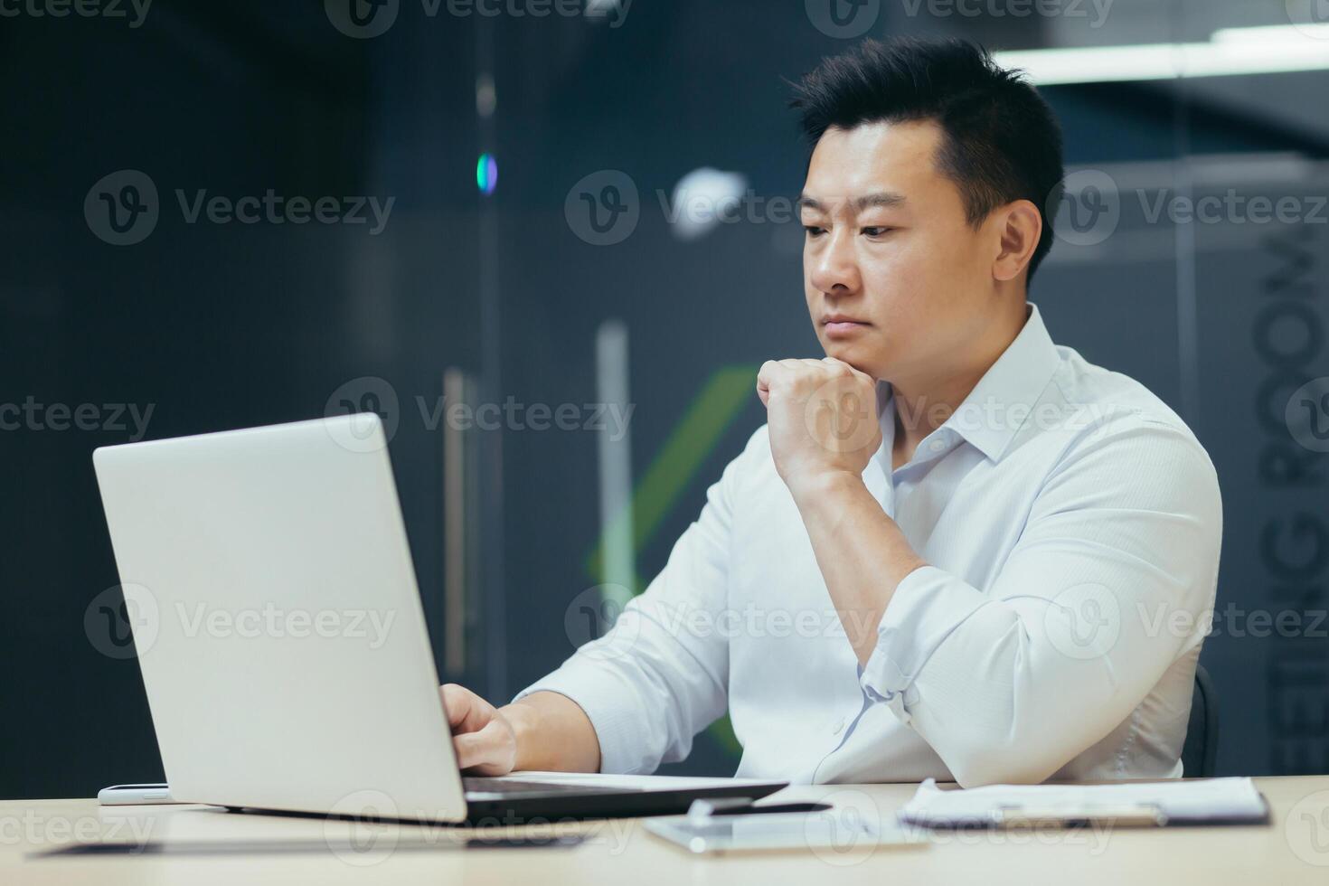Pensive and serious asian businessman working in office, thinking over projector, working with laptop. photo