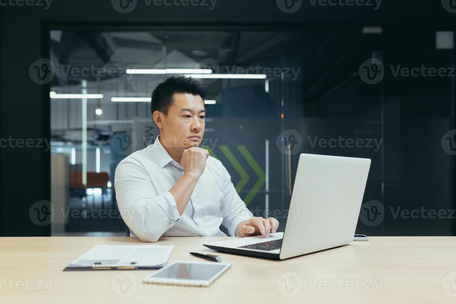 Pensive and serious asian businessman working in office, thinking over projector, working with laptop. photo