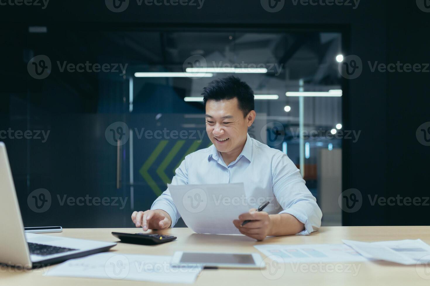 Young Asian male accountant working with documents and calculator. Sitting at a desk with a laptop in a modern office photo