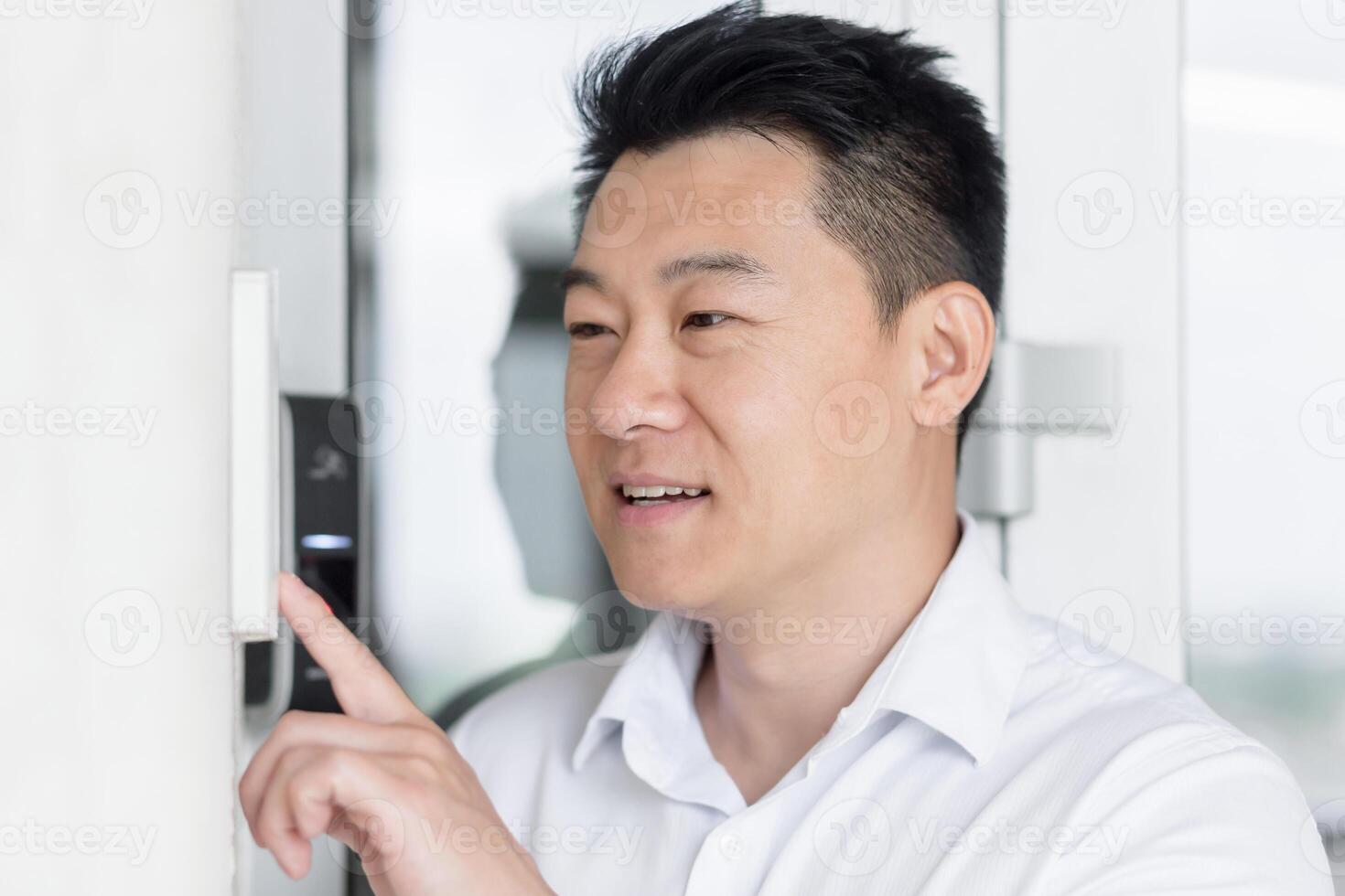 Close-up photo. Portrait of a young handsome Asian man, calling the intercom of the house, pressing the button, waiting for the door to open. photo