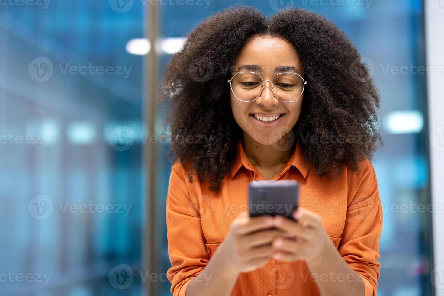 Young woman businesswoman smiling using her tphone. She appears engaged and happy with her device, capturing a moment of productivity and connection in a modern office environment. photo