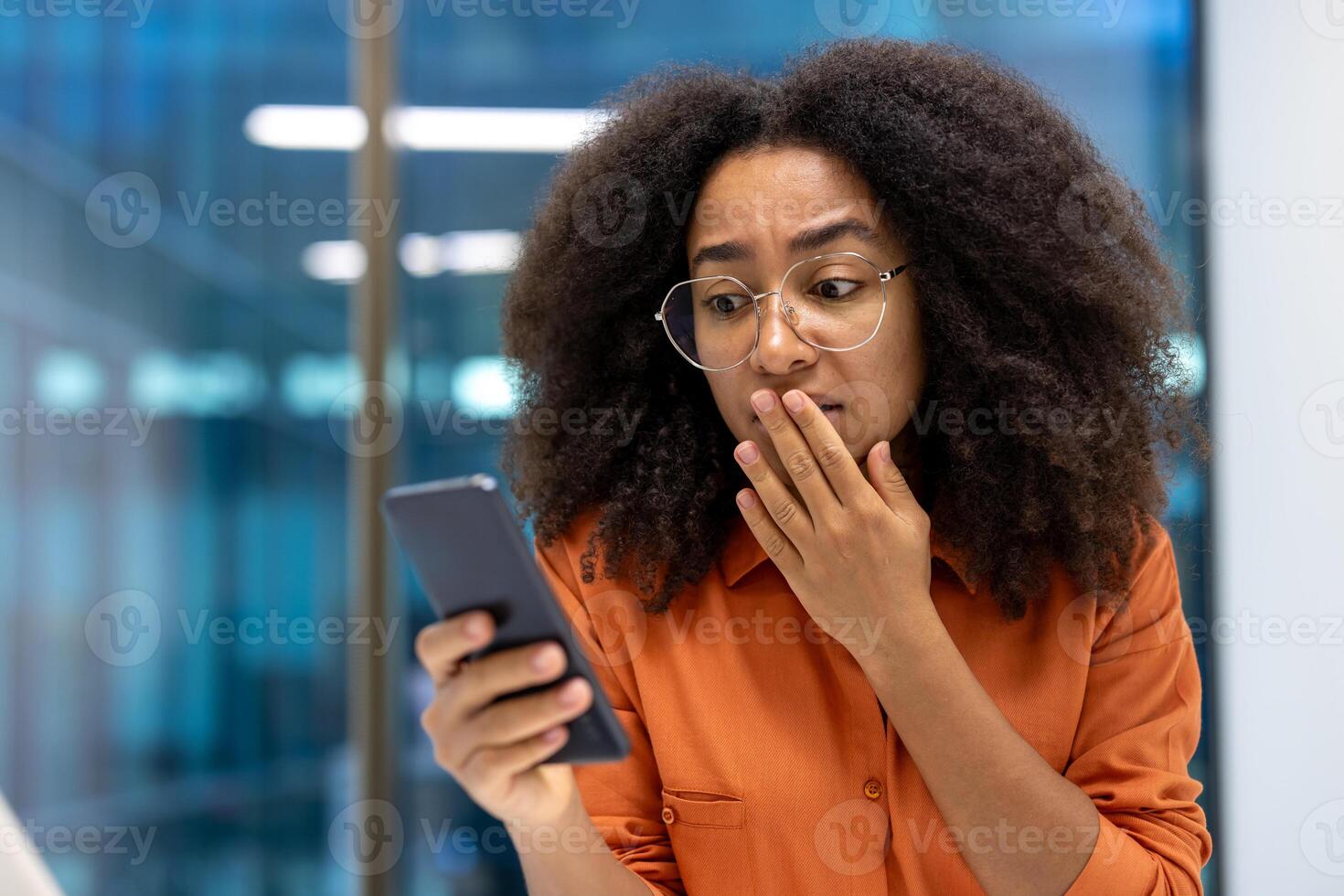 A young businesswoman in an office setting reacts with surprise while looking at her phone. Her expression conveys a sense of shock or unexpected news. photo