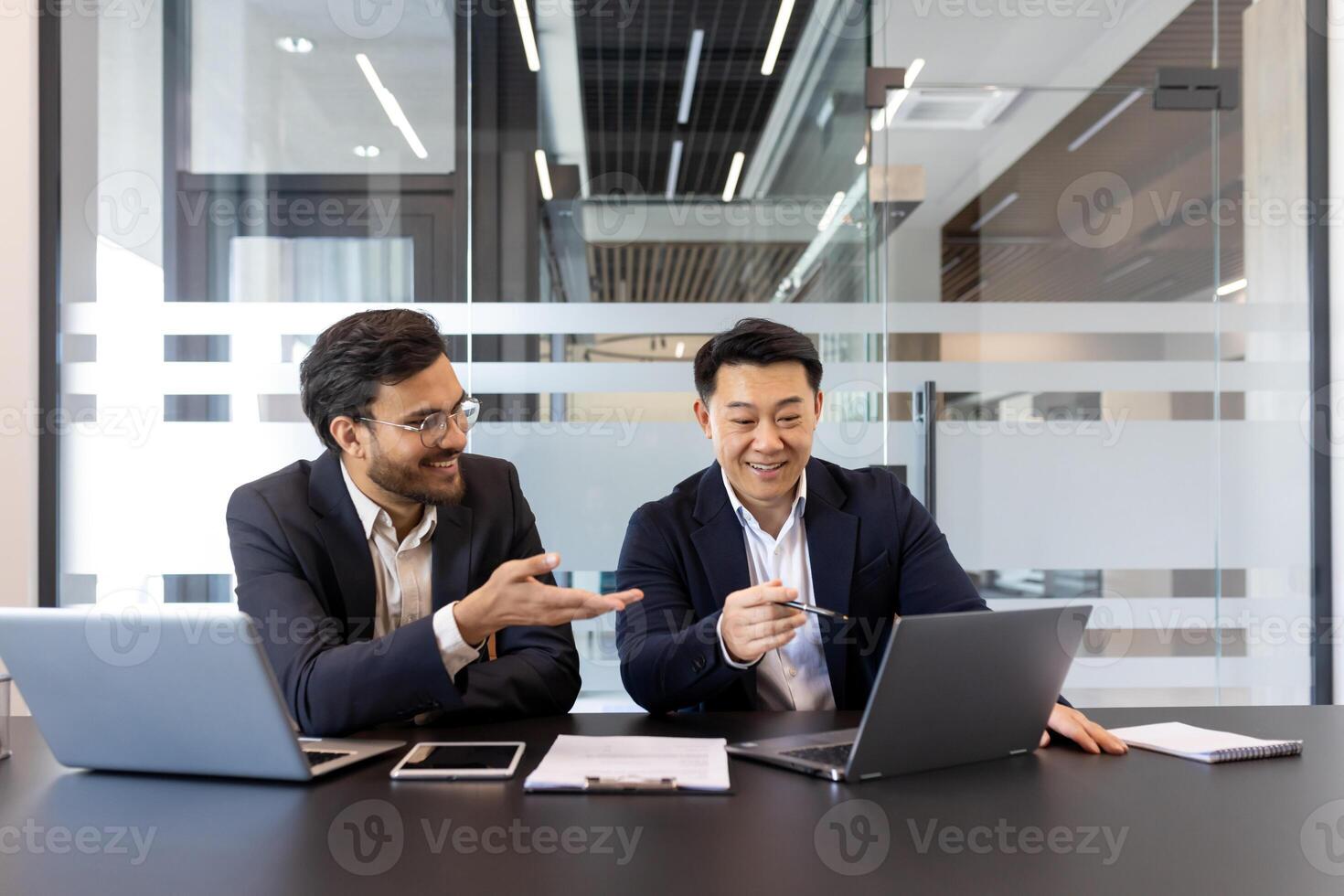Two businessmen are engaged in a collaborative meeting in a contemporary office setting. They are using laptops and documents, creating a dynamic and professional atmosphere for business planning photo