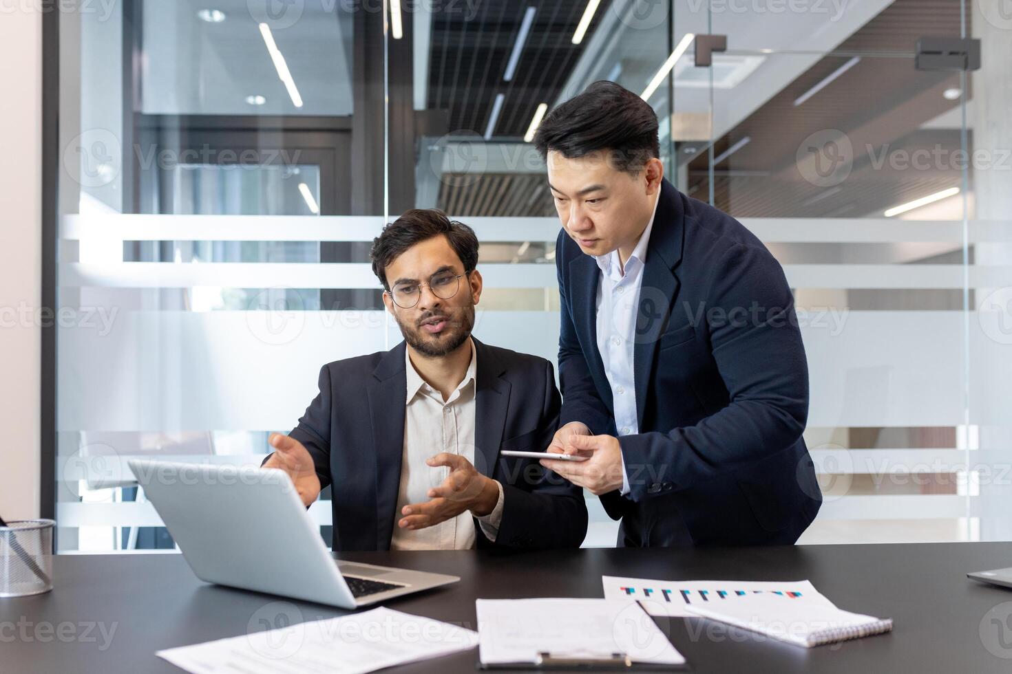 Two professionals in modern office collaborating on project, using laptop and smartphone. Discussing data for successful business outcomes and effective team collaboration. photo