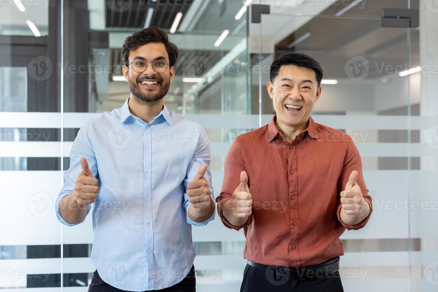 Two smiling men in an office setting, expressing positivity with thumbs up gestures, symbolizing success and teamwork. The image conveys a friendly and professional atmosphere photo