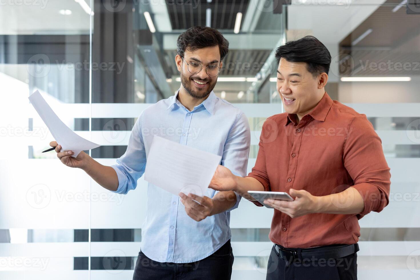 Two colleagues collaborating on project plans while reviewing documents and using tablet. Emphasis on teamwork, communication, and productive office environment with digital and print media. photo