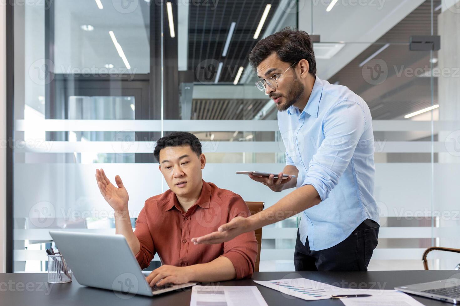 In a modern office, two colleagues are engaged in a discussion. One holds a smartphone while the other uses a laptop. The scene captures the essence of collaboration and teamwork. photo