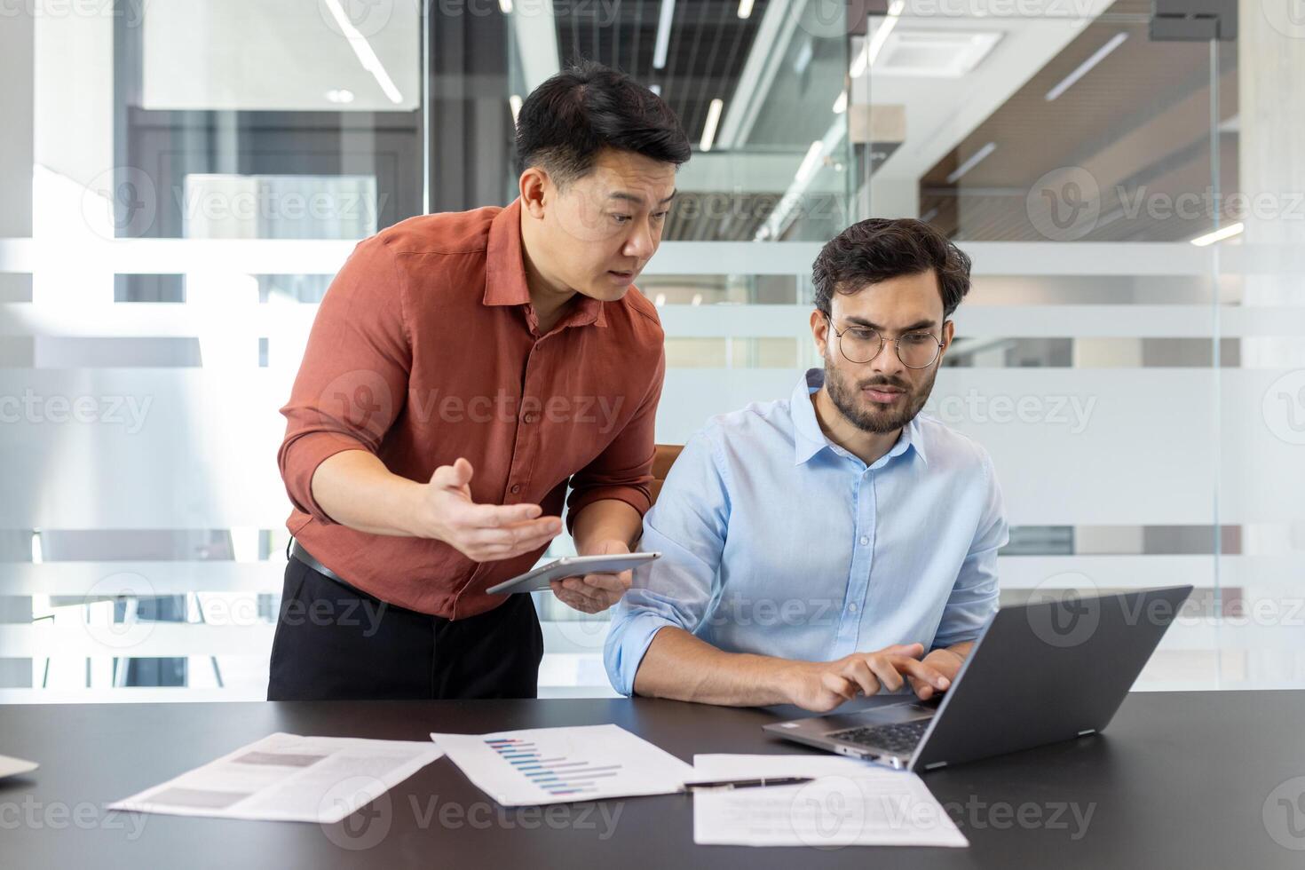 Colleagues collaborating on business project in office, using laptop and documents. Focus on teamwork, technology, and communication in workplace. People engaged in discussion to achieve goals. photo