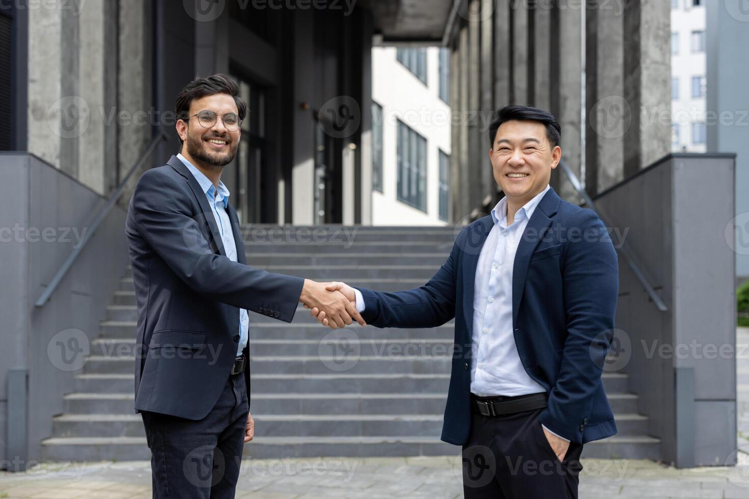 Two business professionals in formal attire exchange a confident handshake outside a modern office. The image captures a moment of agreement and partnership, symbolizing connection and success. photo