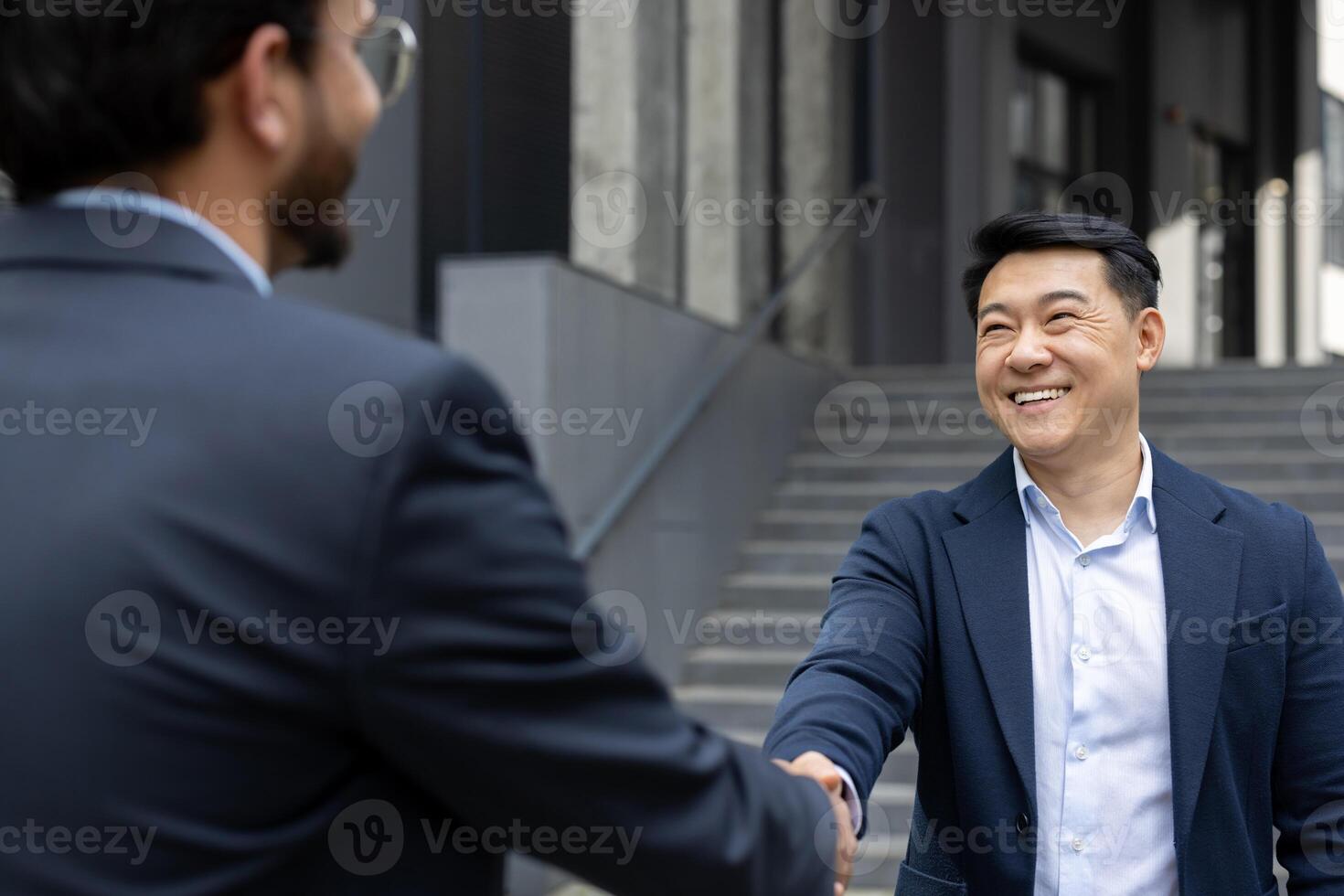 Two business professionals in formal attire shaking hands, symbolizing a successful partnership. The outdoor setting and bright smiles convey trust, connection, and collaboration. photo