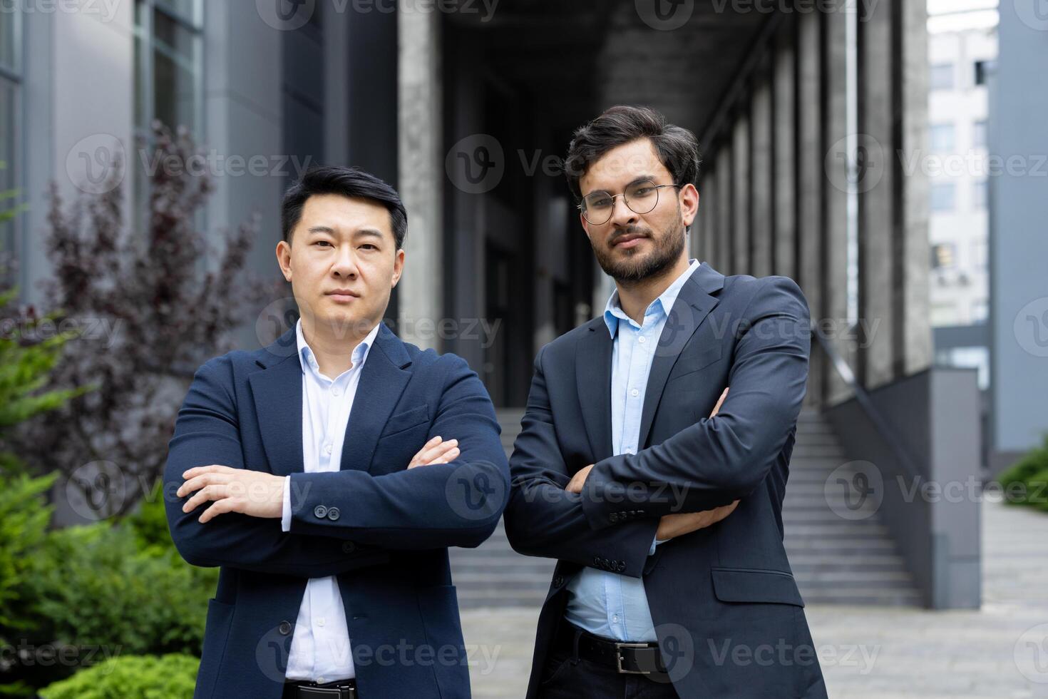Confident business professionals outside modern office building with arms crossed. They display determination and teamwork in professional attire, embodying leadership and success. photo