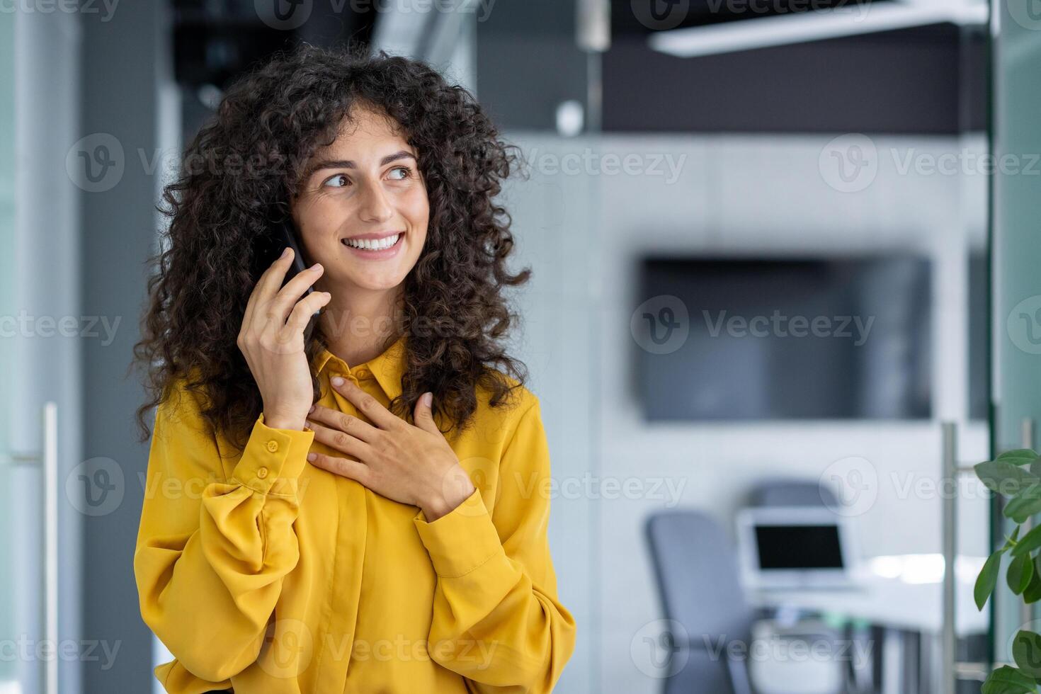 Professional woman in yellow blouse having joyful phone conversation in office, showcasing confidence and happiness. Captures essence of modern communication and business success. photo