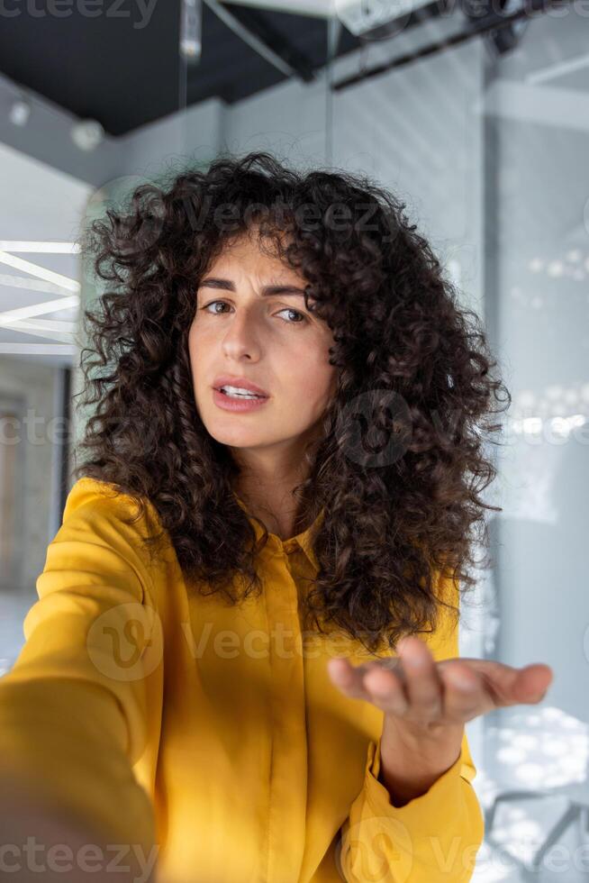 Confident woman gesturing while taking selfie with smartphone. Indoors setting adds modern and casual vibe to image. photo