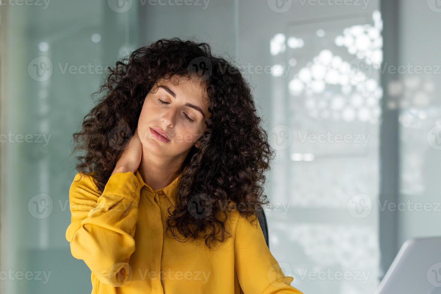 A woman in an office setting is experiencing neck pain, possibly due to poor posture or stress. Her expression suggests discomfort, reflecting a common workplace issue. photo