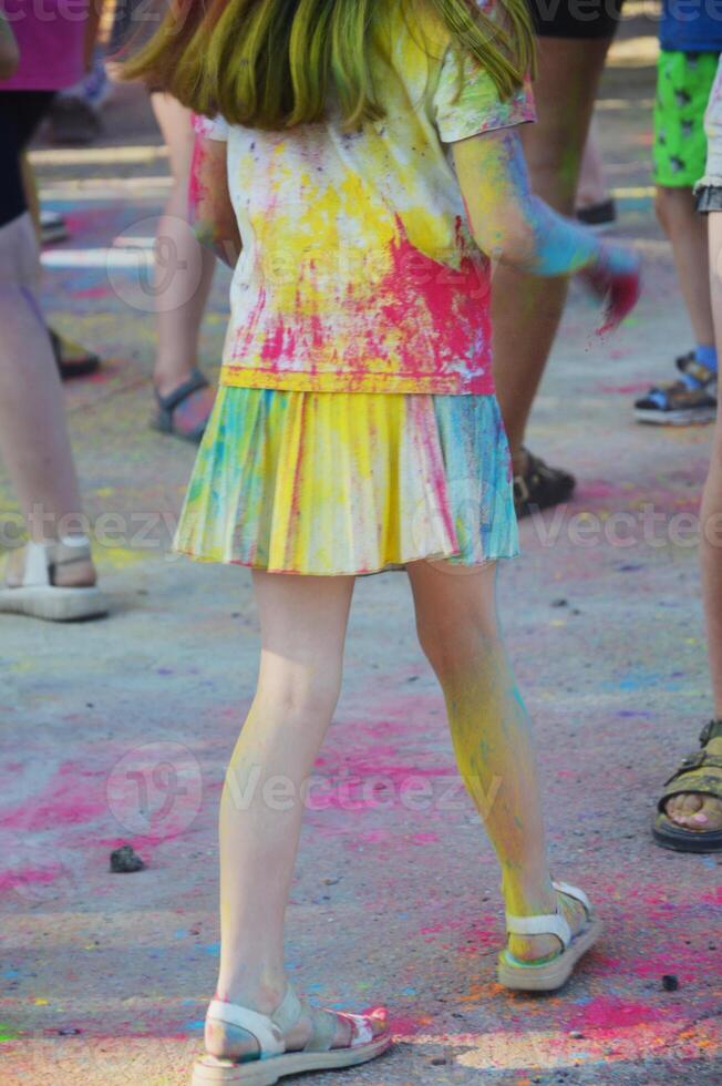 The girl's white T-shirt and skirt are stained with multi-colored paint. Festival of colors. photo