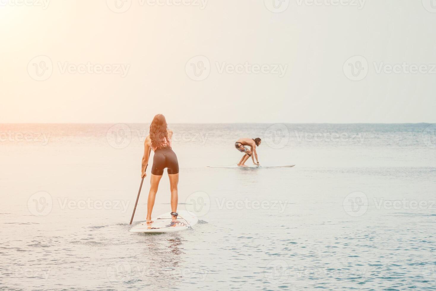Sea woman and man on sup. Silhouette of happy young woman and man, surfing on SUP board, confident paddling through water surface. Idyllic sunset. Active lifestyle at sea or river. photo
